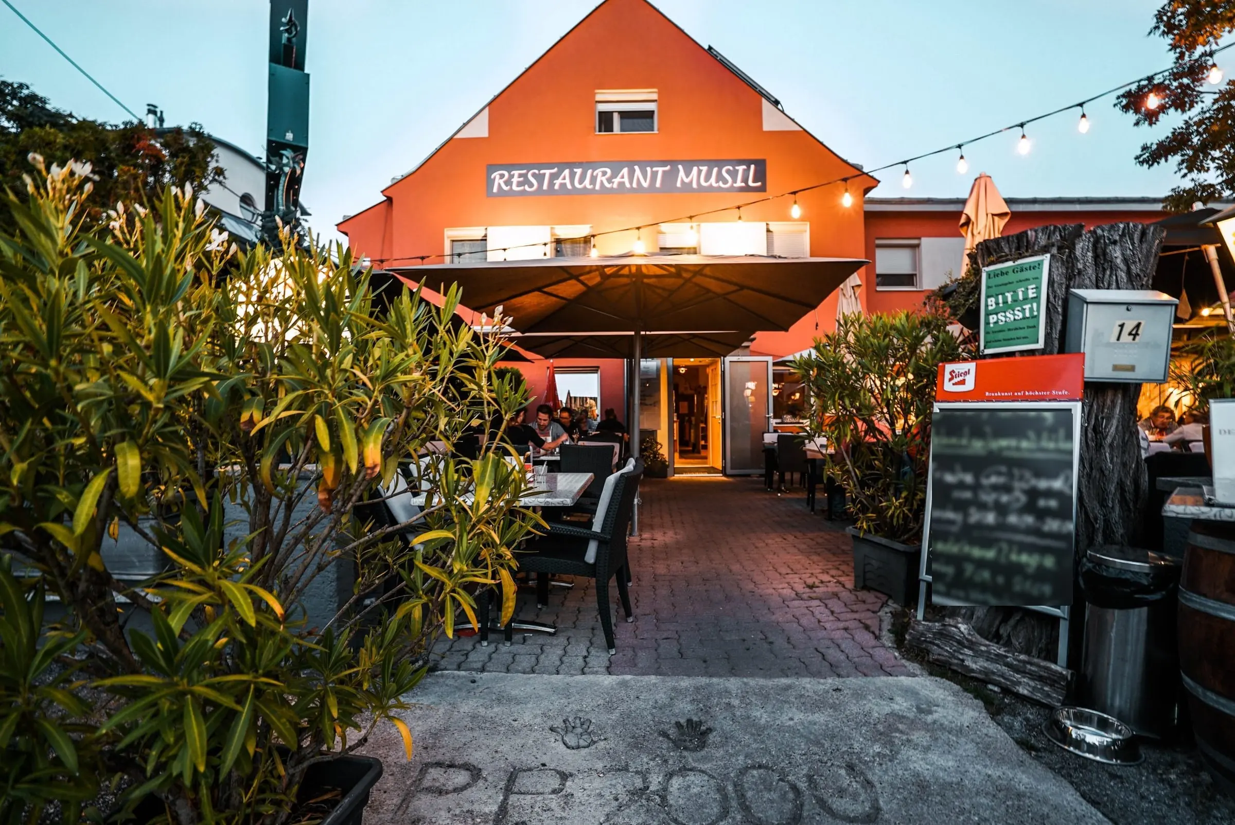 Das Restaurant Musil in der Braillegasse am Abend, mit orangefarbener Fassade und Lichterketten im Gastgarten.