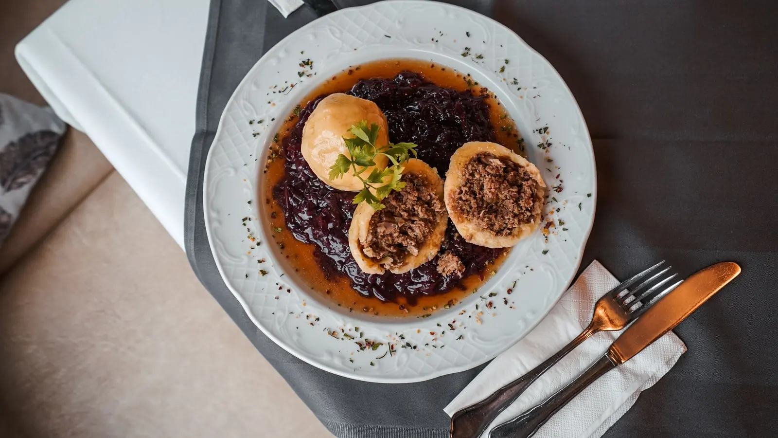 Knödel auf Rotkraut mit Sauce, angerichtet auf einem weißen Teller.
